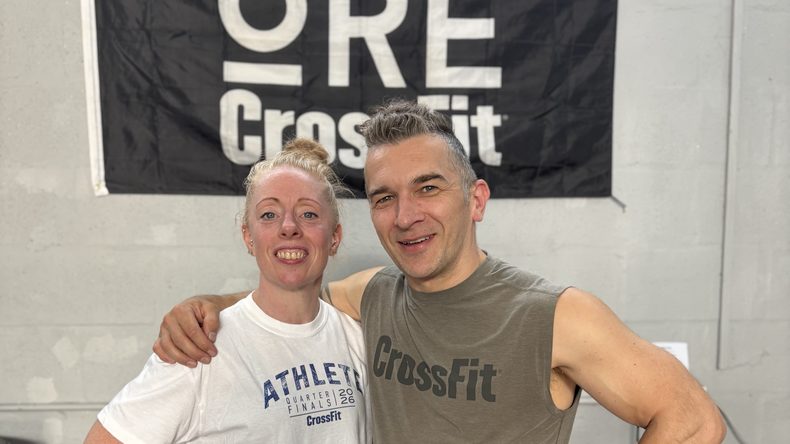 Coaches Vic and Adam, both 50, smiling in front of the ORE CrossFit banner at the gym in Telford